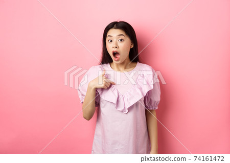 Surprised asian girl gasping wondered, pointing at herself, being chosen or picked, standing in dress against pink background 74161472
