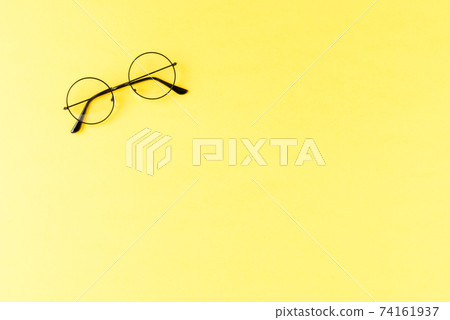 Black framed eyeglasses on yellow table. Top view 74161937