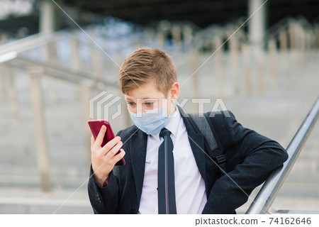 Schoolboy walks out of school wearing protective mask in a city Schoolboy walks out of school wearing protective mask in a city 74162646