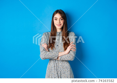 Elegant caucasian girl in dress cross arms on chest, standing on blue background 74163582