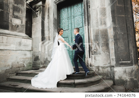 Lovely happy wedding couple, bride with long white dress posing in beautiful city 74164076