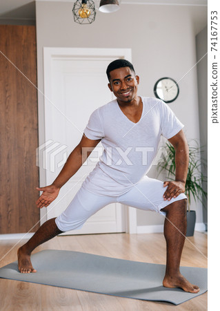 Cheerful African-American fitness instructor making sport exercise standing on yoga mat Cheerful African-American fitness instructor making sport exercise standing on yoga mat 74167753