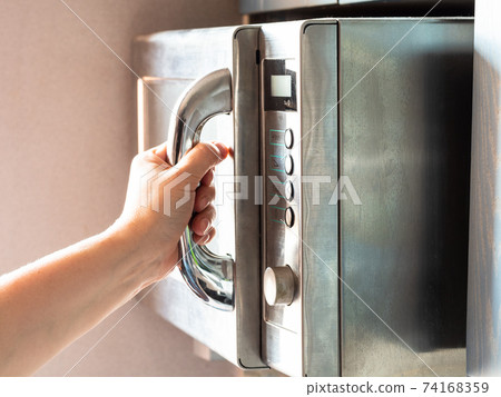 female hand opens an old microwave oven at home female hand opens an old microwave oven at home 74168359
