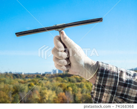 male hand wipes a home window glass by squeegee 74168368