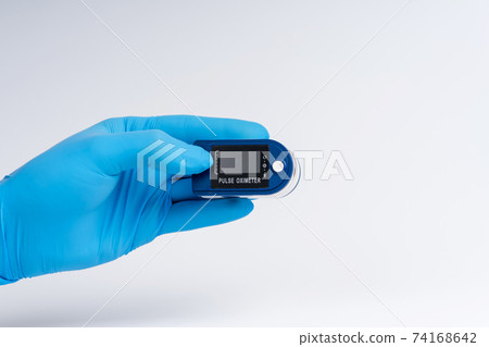 Pulse oximeter on a white background. A hand in a medical glove holds a device for health diagnostics 74168642
