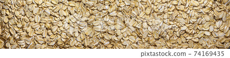 A close-up of a spelt cereal flakes for breakfast. Panoramic background of oat flakes. A close-up of a spelt cereal flakes for breakfast. Panoramic background of oat flakes. 74169435