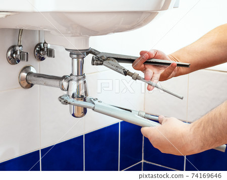 man adjusts two old pipe-wrenches to install sink 74169646
