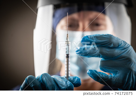 Doctor or Nurse Holding Medical Syringe with Needle AGainst Dark Background Doctor or Nurse Holding Medical Syringe with Needle AGainst Dark Background 74172075