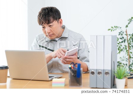 A man in work clothes hitting a calculator at work A man in work clothes hitting a calculator at work 74174851