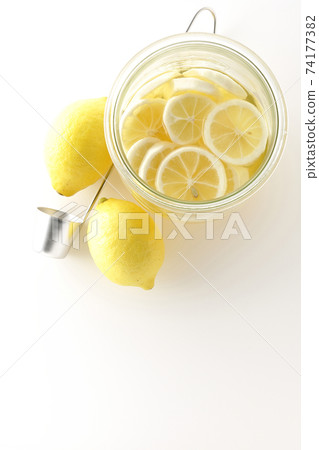 Photographed undiluted solution of lemon squash and lemonade in a storage bottle, ladle and lemon on a white background (overhead view) 74177382