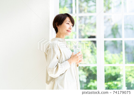 Woman drinking water by the window Woman drinking water by the window 74179075