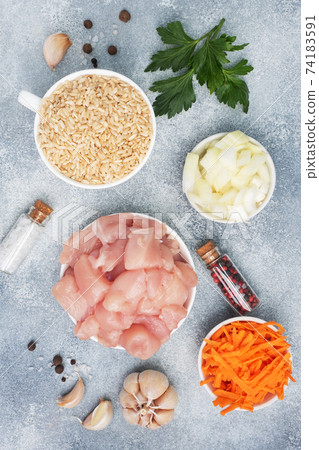 Raw ingredients for cooking pilaf, Brown rice and chicken fillet, grated carrots and chopped onions, pepper tomato garlic herbs and spices. Gray background, top view. Raw ingredients for cooking pilaf, Brown rice and chicken fillet, grated carrots and chopped onions, pepper tomato garlic herbs and spices. Gray background, top view. 74183591