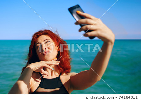 Red-haired woman takes selfie on smartphone camera. Red-haired woman takes selfie on smartphone camera. 74184011
