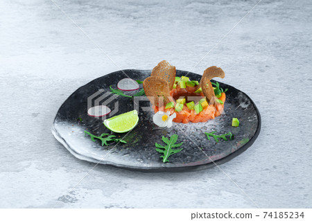 Portion of fresh salmon and avocado tartar on black plate Portion of fresh salmon and avocado tartar on black plate 74185234