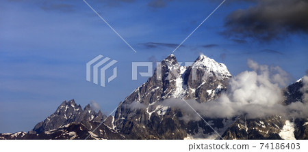 Panoramic view on high rocky mountains with snow and glacier in clouds 74186403