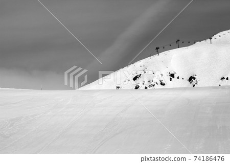 Black and white view on snowy ski slope and chair-lift at gray winter day Black and white view on snowy ski slope and chair-lift at gray winter day 74186476