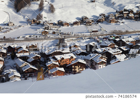 Snowy ski slope in high winter mountains and sunlit village at background Snowy ski slope in high winter mountains and sunlit village at background 74186574