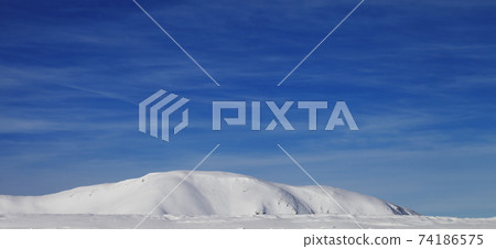 Panoramic view on snowy ski slope at high winter mountains and sunlit cloudy sky Panoramic view on snowy ski slope at high winter mountains and sunlit cloudy sky 74186575