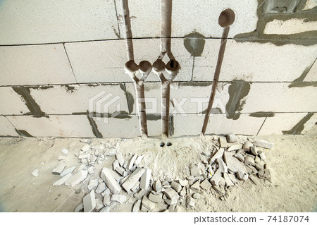 Deep grooves and holes in white brick wall made for installation of electrical cables. Deep grooves and holes in white brick wall made for installation of electrical cables. 74187074