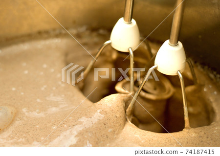 Closeup of electrical blender whipping in bowl chocolate cream for cake, ice cream or dessert. Kitchen bakery equipment, homemade baking. 74187415