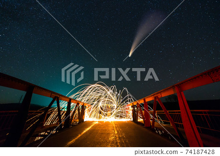 Long exposure of spinning steel wool in abstract circle making firework showers of yellow glowing sparks on a bridge with dark night starry sky above. Long exposure of spinning steel wool in abstract circle making firework showers of yellow glowing sparks on a bridge with dark night starry sky above. 74187428