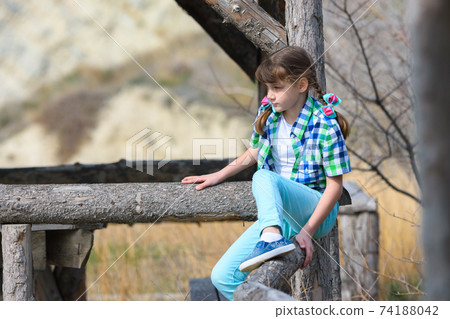 A girl tries to sit on a fence made of a thick wooden frame 74188042