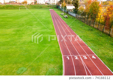 Aerial view of sports stadium with red running tracks with numbers on it and green grass football field. Aerial view of sports stadium with red running tracks with numbers on it and green grass football field. 74188112
