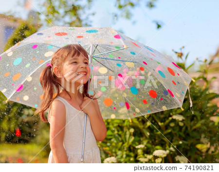 Happy little girl in garden under the summer rain with an umbrella. Happy little girl in garden under the summer rain with an umbrella. 74190821