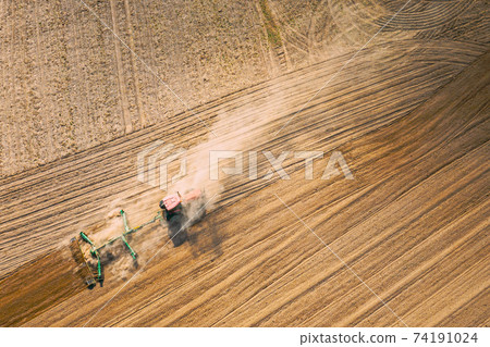 Aerial View. Tractor Plowing Field. Beginning Of Agricultural Spring Season. Cultivator Pulled By A Tractor In Countryside Rural Field Landscape. Dust Rises From Under Plows Aerial View. Tractor Plowing Field. Beginning Of Agricultural Spring Season. Cultivator Pulled By A Tractor In Countryside Rural Field Landscape. Dust Rises From Under Plows 74191024