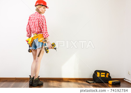 Woman wearing helmet, toolbelt about to drill wall Woman wearing helmet, toolbelt about to drill wall 74192784