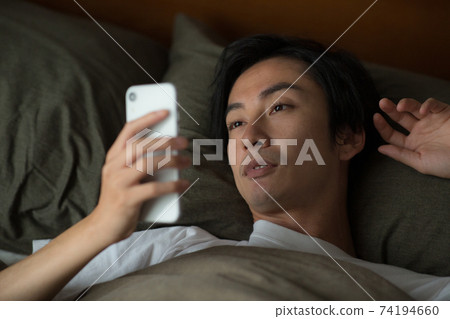 男人在床上看著智能手機 74194660