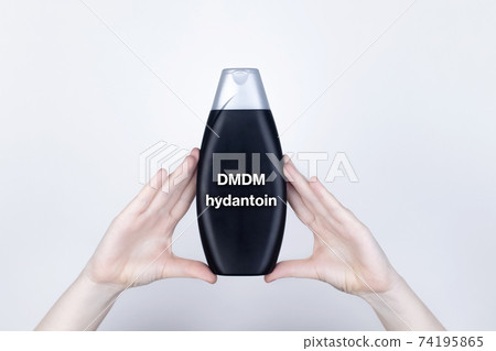 Chemical components on the shampoo label: DMDM hydantoin. Female hands hold the jar on which indicates the harmful ingredient. White background, place for your text 74195865