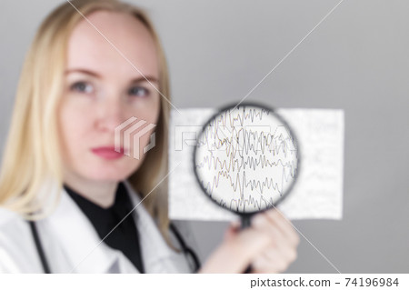 A neurologist with a magnifying glass examines an encephalogram of a patient brain. Schedule of electroencephalograms study of brain currents for signs of epilepsy and pathologies 74196984