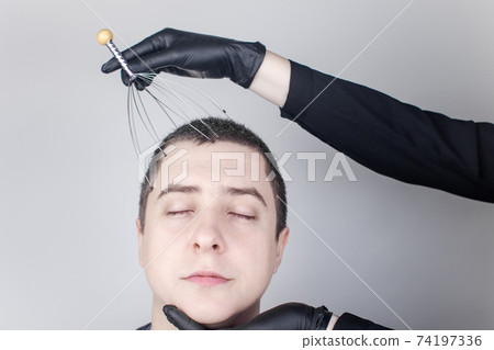 A man is given a head massage with a capillary massager in the salon. The client's face shows relaxation and joy. The concept of anti-stress massage and the provision of services by a masseur. A man is given a head massage with a capillary massager in the salon. The client's face shows relaxation and joy. The concept of anti-stress massage and the provision of services by a masseur. 74197336