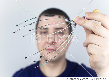 A man on a white background makes himself a head massage with a capillary massager. Self-help, anti-stress and relaxation concept 74197344