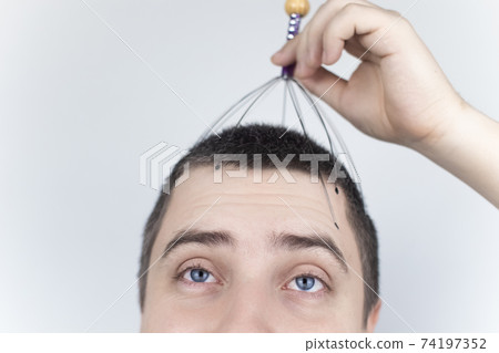 A man on a white background makes himself a head massage with a capillary massager. Self-help, anti-stress and relaxation concept A man on a white background makes himself a head massage with a capillary massager. Self-help, anti-stress and relaxation concept 74197352