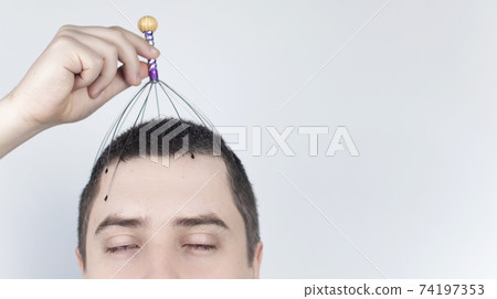 A man on a white background makes himself a head massage with a capillary massager. Self-help, anti-stress and relaxation concept 74197353