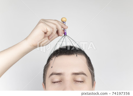 A man on a white background makes himself a head massage with a capillary massager. Self-help, anti-stress and relaxation concept A man on a white background makes himself a head massage with a capillary massager. Self-help, anti-stress and relaxation concept 74197356