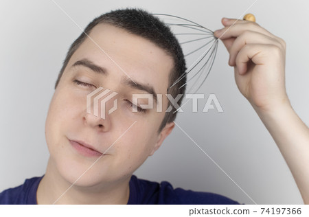 A man on a white background makes himself a head massage with a capillary massager. Self-help, anti-stress and relaxation concept A man on a white background makes himself a head massage with a capillary massager. Self-help, anti-stress and relaxation concept 74197366