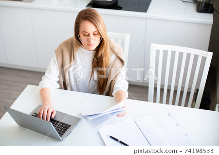 Online work concept. Woman works online in front of a laptop monitor. She fills out tax forms or pays bills. Photo in home interior. Online work concept. Woman works online in front of a laptop monitor. She fills out tax forms or pays bills. Photo in home interior. 74198533