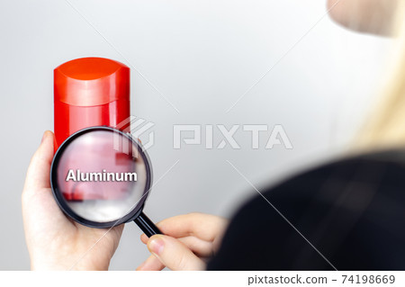A woman examines the harmful ingredients of the antiperspirant a magnifying glass. Dry stick deodorant stick with Aluminum. The concept of hazardous substances in cosmetics and household chemicals 74198669
