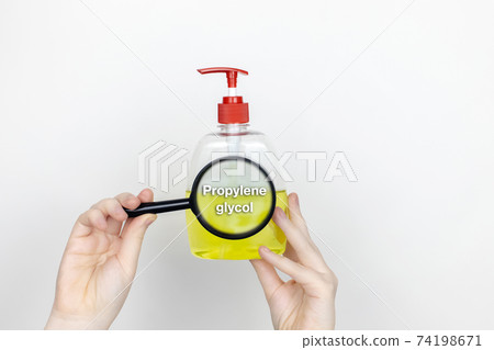 A woman examines the harmful ingredients of the liquid soap a magnifying glass. Harmful composition of ingredients. Means with Propylene glycol 74198671