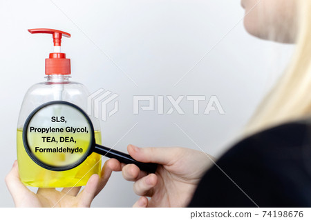 A woman examines the harmful ingredients of the liquid soap a magnifying glass. Harmful composition of ingredients. Means with SLS, Propylene Glycol, TEA, DEA, Formaldehyde. A woman examines the harmful ingredients of the liquid soap a magnifying glass. Harmful composition of ingredients. Means with SLS, Propylene Glycol, TEA, DEA, Formaldehyde. 74198676