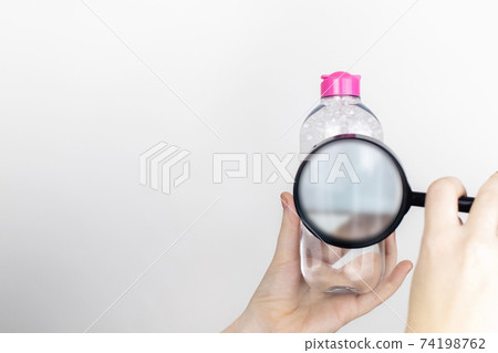 A woman examines the harmful ingredients of the micellar waterthrough a magnifying glass. Place for your text. The concept of hazardous substances in cosmetics and household chemicals A woman examines the harmful ingredients of the micellar waterthrough a magnifying glass. Place for your text. The concept of hazardous substances in cosmetics and household chemicals 74198762
