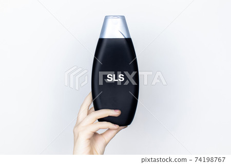 Chemical components on the shampoo label:  Sodium Lauryl Sulfate (sls, sles). A hand holds a jar and a magnifier, where the harmful ingredients of a detergent are written in close up. 74198767