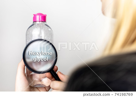 A woman examines the harmful ingredients of the micellar waterthrough a magnifying glass. Means with hexylene glycol. The concept of hazardous substances in cosmetics and household chemicals A woman examines the harmful ingredients of the micellar waterthrough a magnifying glass. Means with hexylene glycol. The concept of hazardous substances in cosmetics and household chemicals 74198769
