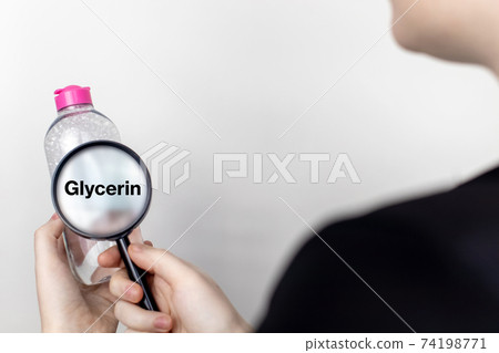 A woman examines the harmful ingredients of the micellar waterthrough a magnifying glass. Means with glycerin. The concept of hazardous substances in cosmetics and household chemicals A woman examines the harmful ingredients of the micellar waterthrough a magnifying glass. Means with glycerin. The concept of hazardous substances in cosmetics and household chemicals 74198771
