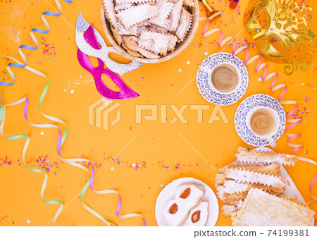 Carnival mask, two cups of aromatic coffee, sweets and confetti on a yellow background. Decor for a 74199381