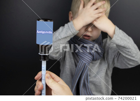 Antipyretic drug for a child. Medicinal syrup in a syringe on the background of a sick boy. The concept of treating children at home. 74200021