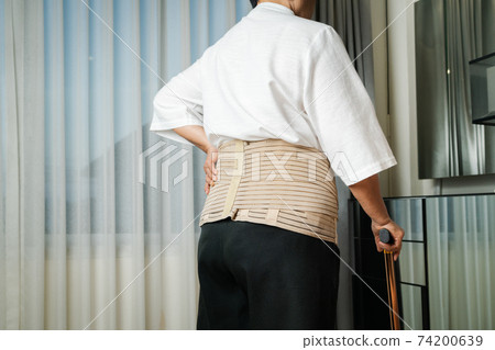 Senior back pain woman with walking stick at home 74200639